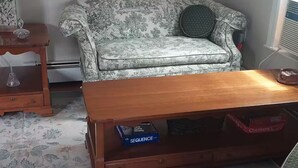 Ein Wohnzimmer mit einem floralen Sofa, einem Holztisch und einem gemusterten Teppich.