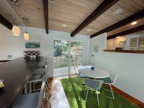 A modern kitchen with a bar area, a dining table with chairs, and a sliding glass door leading to a garden. - Retromoderninthewoods steps from the best trails in the Linville gorge wildernes (Newland)