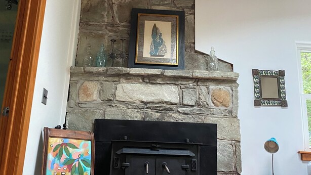 A stone fireplace with a framed artwork above it, a wooden chair in front, and a small table with a lamp to the right. - Retromoderninthewoods steps from the best trails in the Linville gorge wildernes (Newland)