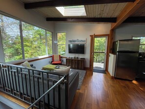 Una cocina moderna con refrigerador empotrado, un comedor con banco y un amplio ventanal con vista a árboles.