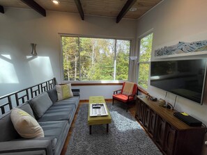 Uma sala de estar com sofá, poltrona, mesa de centro e televisão sobre um suporte.
