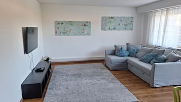 Ein modernes Wohnzimmer mit einem grauen Sofa, einem Flachbildfernseher und zwei floralen Wandbildern.