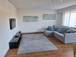 A modern living room with a grey sofa, a flat-screen TV, and two floral wall art pieces.