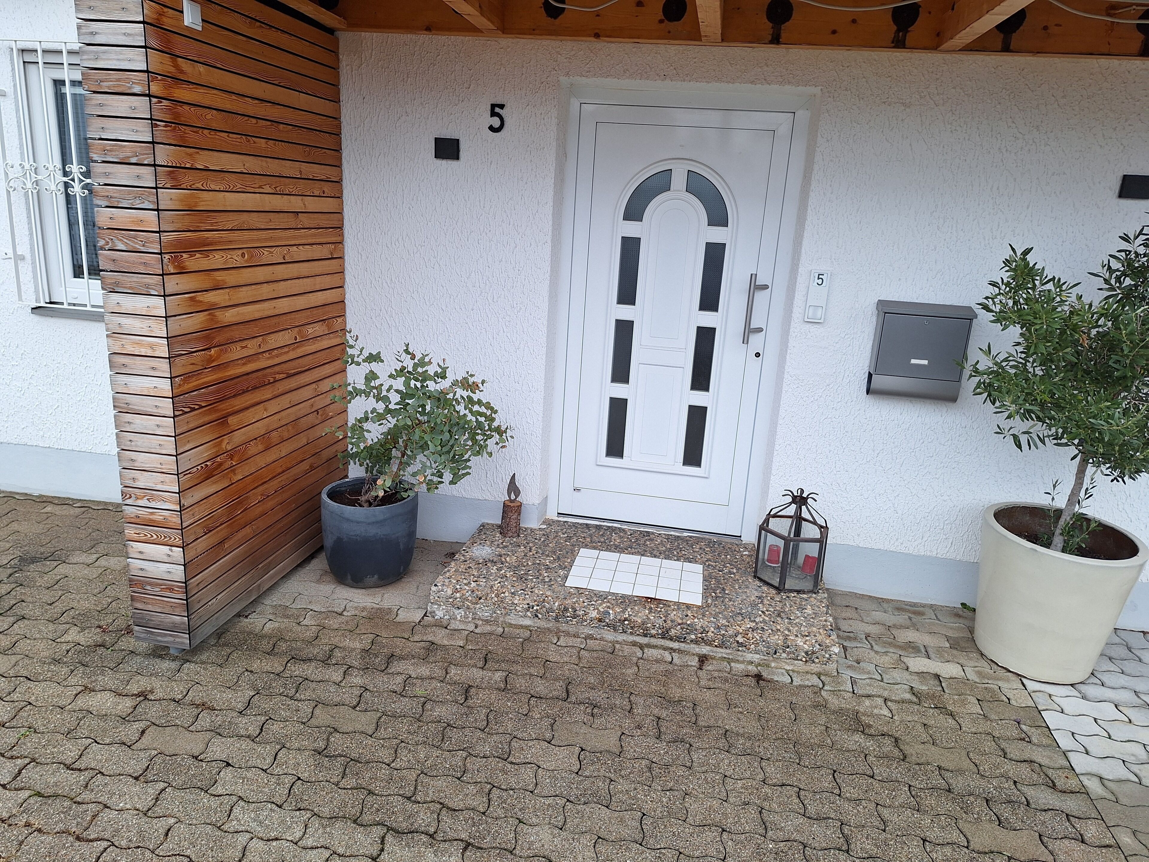 Ein Gebäudeeingang mit einer Wand aus Holzpaneelen, einer weißen Tür mit der Nummer 5 und zwei Blumentöpfen.