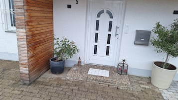 Ein Gebäudeeingang mit einer Wand aus Holzpaneelen, einer weißen Tür mit der Nummer 5 und zwei Blumentöpfen.