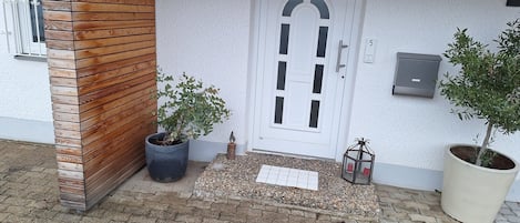 A building entrance with a wooden panel wall, a white door with the number 5, and two potted plants.