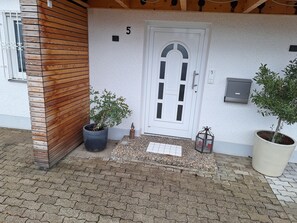 A building entrance with a wooden panel wall, a white door with the number 5, and two potted plants.