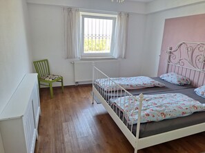 Ein Schlafzimmer mit einem Einzelbett, einem Sessel, einem Heizkörper und einem Fenster mit Vorhängen.