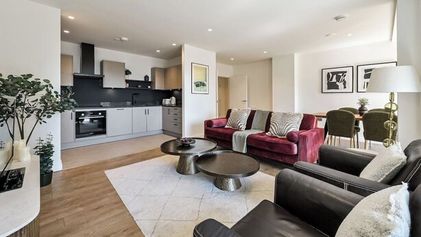 Ein modernes Wohnzimmer mit einem roten Sofa, zwei runden Couchtischen und einer Küche im Hintergrund.