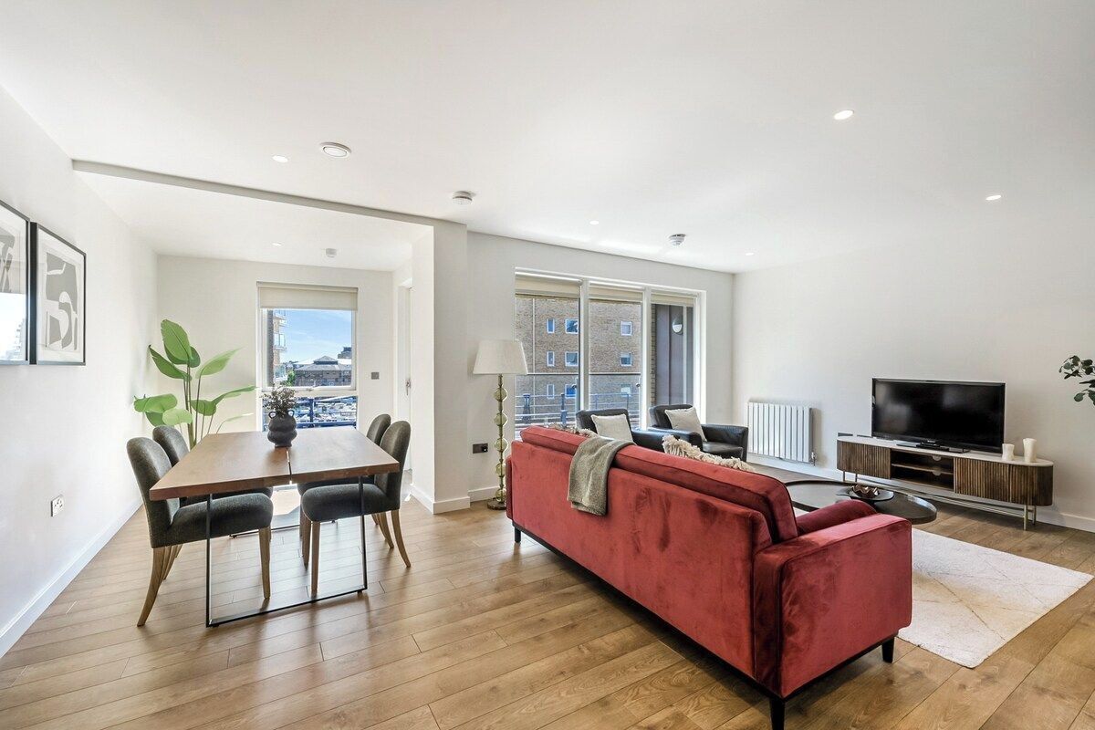 A modern living room with a dining area, a red sofa, a TV, and a large window.