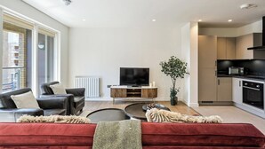 Ein modernes Wohnzimmer mit einem roten Sofa, schwarzen Ledersesseln, einem Flachbildfernseher und einem Essbereich mit einer Mikrowelle.