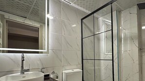 Et moderne badeværelse med en rund vask, toilet og glas brusekabine.