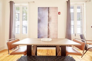 Ein Zimmer mit einem Holztisch, vier Ledersesseln, einem großen abstrakten Gemälde und einem Fenster mit Vorhängen.