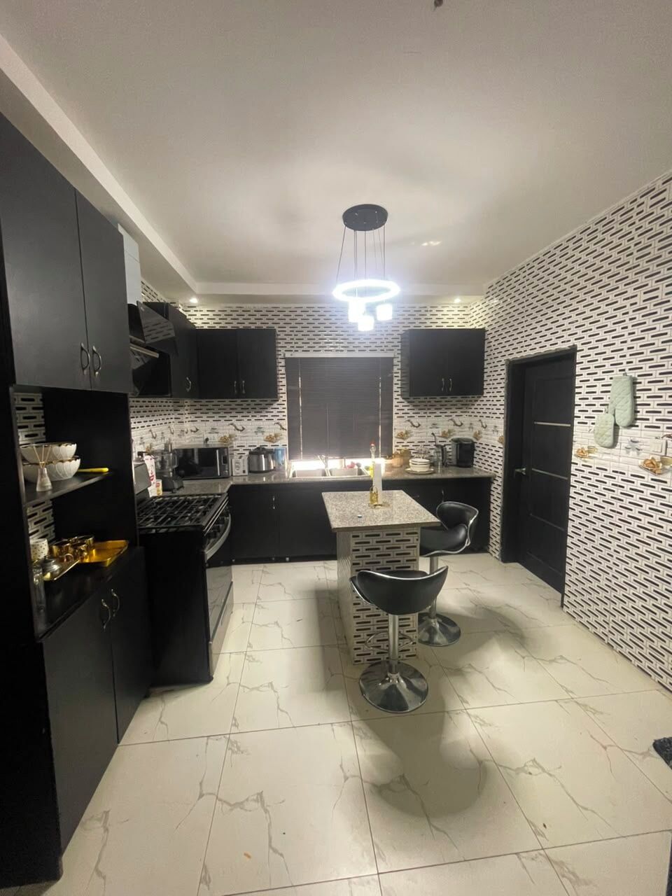 A compact kitchen with black cabinets, a marble countertop, and a central island with stools.