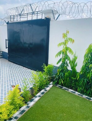A modern building with a large black door, a tiled patio, and a small garden with various plants. - Peaceful 4-bedroom house with AC in charming Old Yundum (Old yundum)
