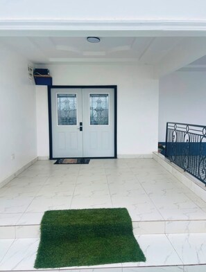 A clean, modern entrance with a double door, a small green rug, and a balcony with a metal railing. - Peaceful 4-bedroom house with AC in charming Old Yundum (Old yundum)