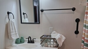 A bathroom with a sink, mirror, towel rack, and a trash can. - Historical Main Street Studio in Charming La Crosse (La Crosse)
