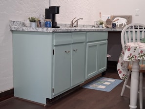 A kitchen with a light blue countertop, a coffee maker, and a sink.