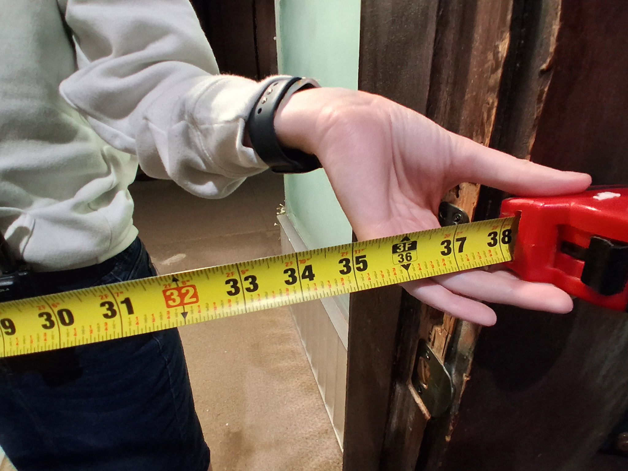 A person measuring a door with a yellow measuring tape.