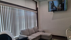 A living room with a sectional sofa, a dark armchair, a television mounted on the wall, and a patterned rug. - Historical Main Street Studio in Charming La Crosse (La Crosse)