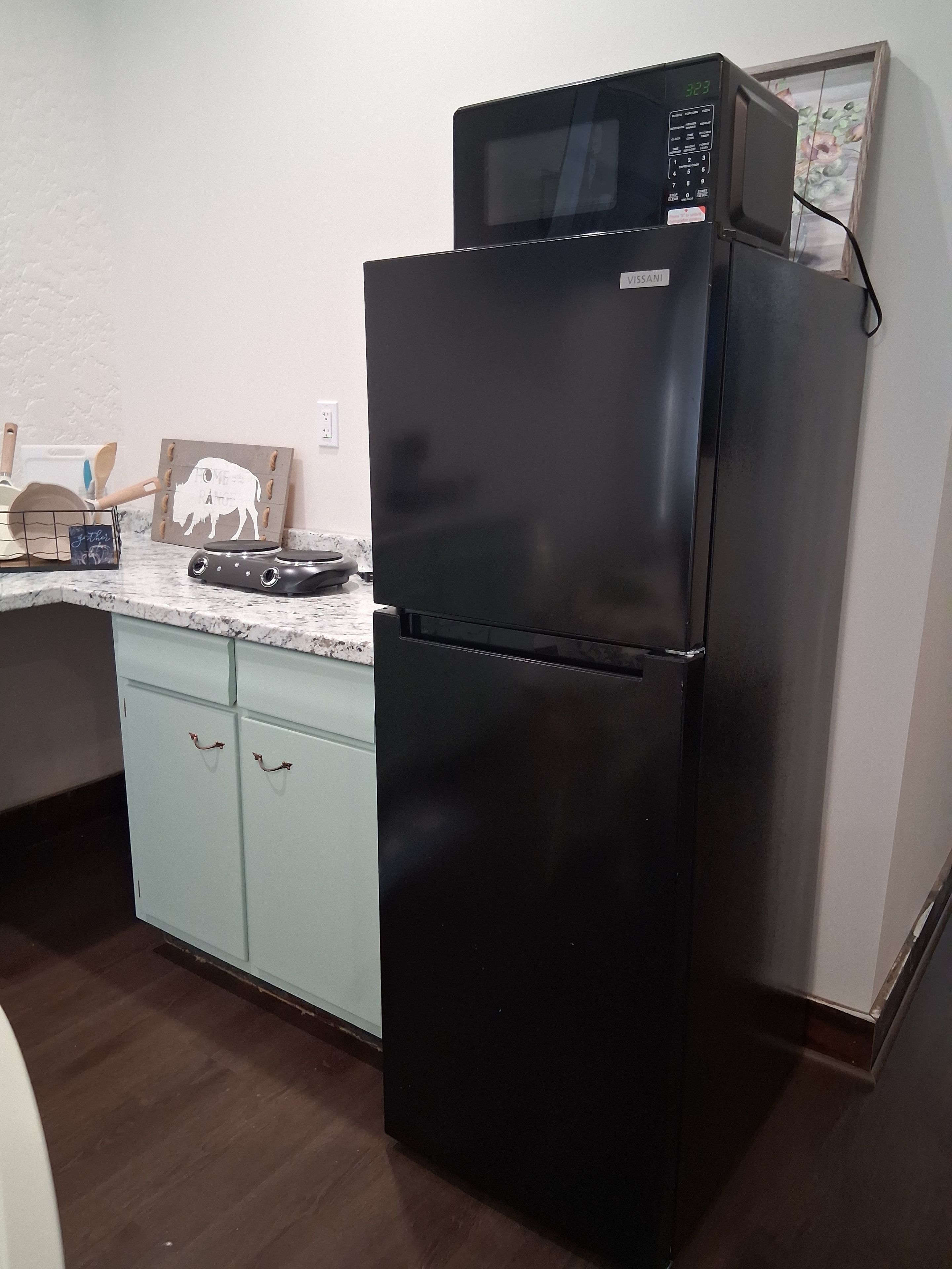 A kitchen with a black refrigerator, a microwave, and a wooden cutting board on the counter.