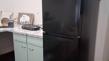 A kitchen with a black refrigerator, a microwave, and a wooden cutting board on the counter.