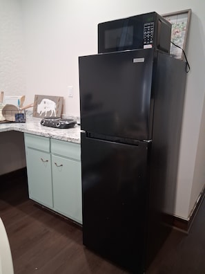 A kitchen with a black refrigerator, a microwave, and a wooden cutting board on the counter.