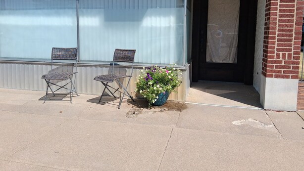 A building with a closed shuttered window, a door, and a small outdoor seating area with two chairs and a potted plant. - Historical Main Street Studio in Charming La Crosse (La Crosse)