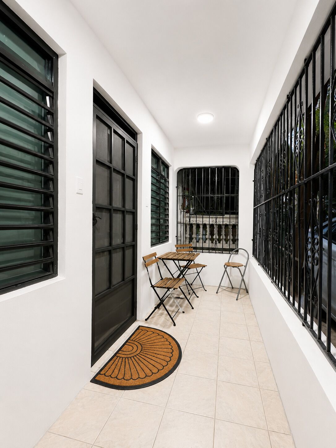 A corridor with a tiled floor, a door with a black metal gate, and a table with chairs.
