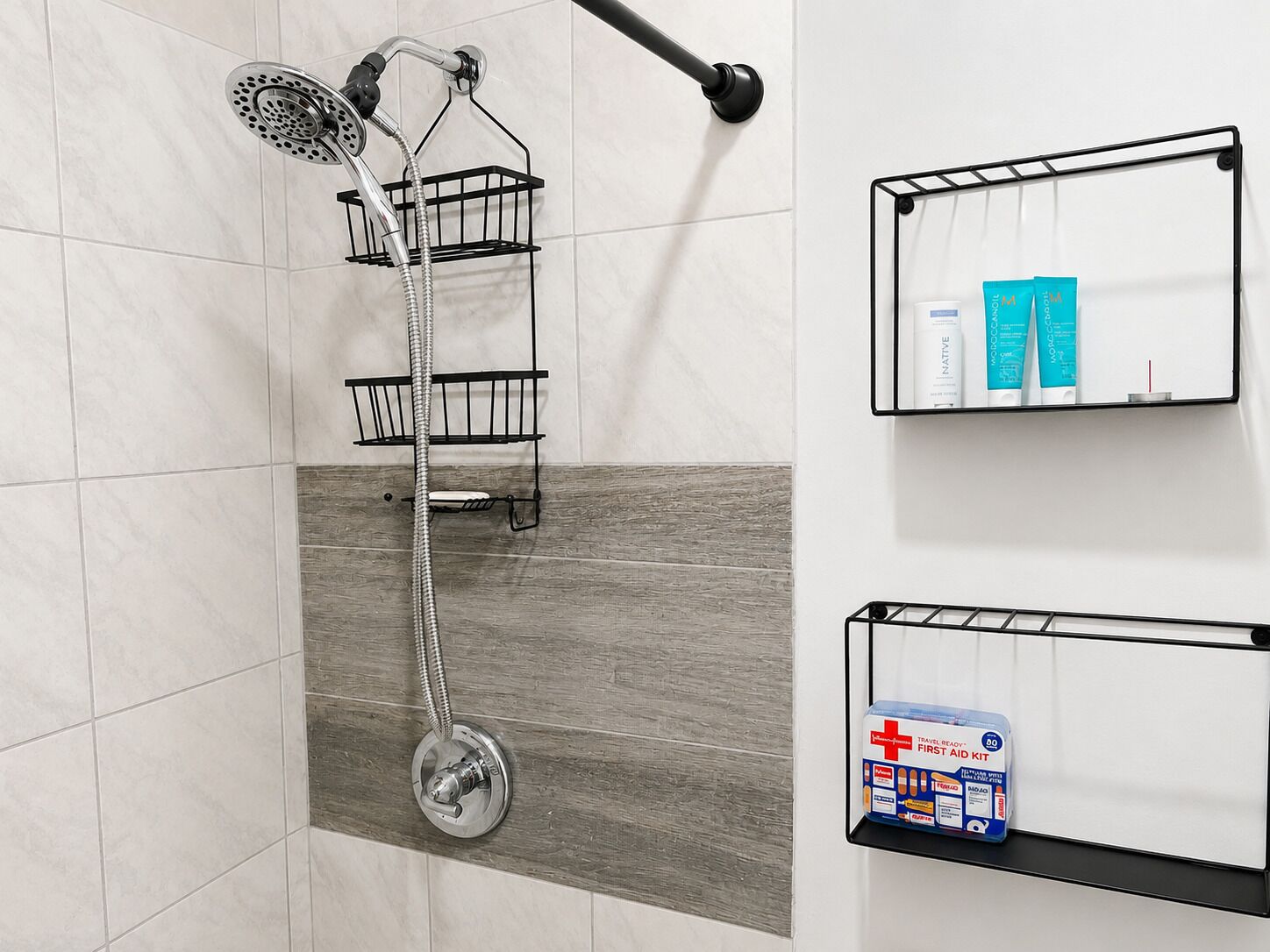 Eine Dusche mit Schlauch, ein Metallgestell, ein Handtuchhalter und ein Ablagefach mit Toilettenartikeln.