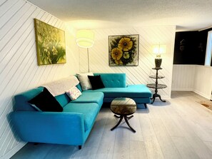 Ein Wohnzimmer mit einem blauen Sofa, einem runden Couchtisch und einem Sonnenblumenbild an der Wand.