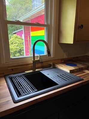 A kitchen with a stainless steel sink, wooden countertop, and a window with a colorful view. - Peaceful Vintage Charm in North Asheville (Asheville)