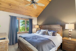 A bedroom with a wooden ceiling fan, a large bed with multiple pillows, a nightstand with a lamp, and a window with curtains. - Sunset Views, Hot Tub, and Firepit in Wintergreen! (Wintergreen Resort)