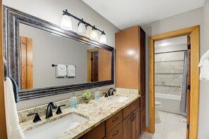 A bathroom with a large mirror, two sinks, a shower, and wooden cabinets. - Sunset Views, Hot Tub, and Firepit in Wintergreen! (Wintergreen Resort)