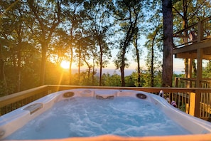 Ein Whirlpool auf einer Holzterrasse mit Blick auf Bäume und den Sonnenuntergang.
