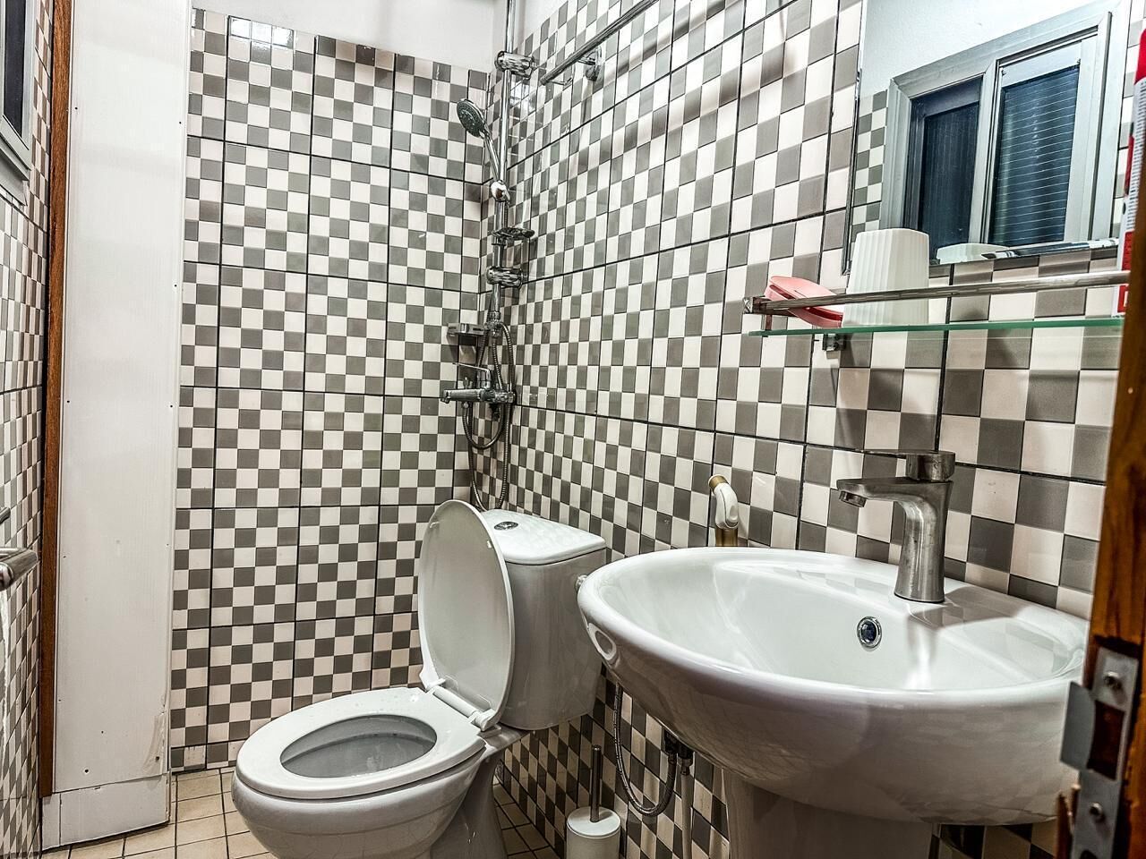 A bathroom with a checkered tile wall, a toilet, a sink, and a shower.