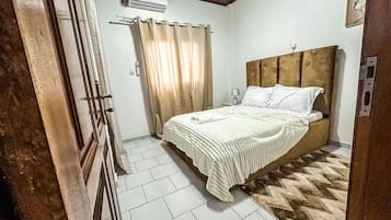 A bedroom with a bed, curtains, a headboard, and a tiled floor.