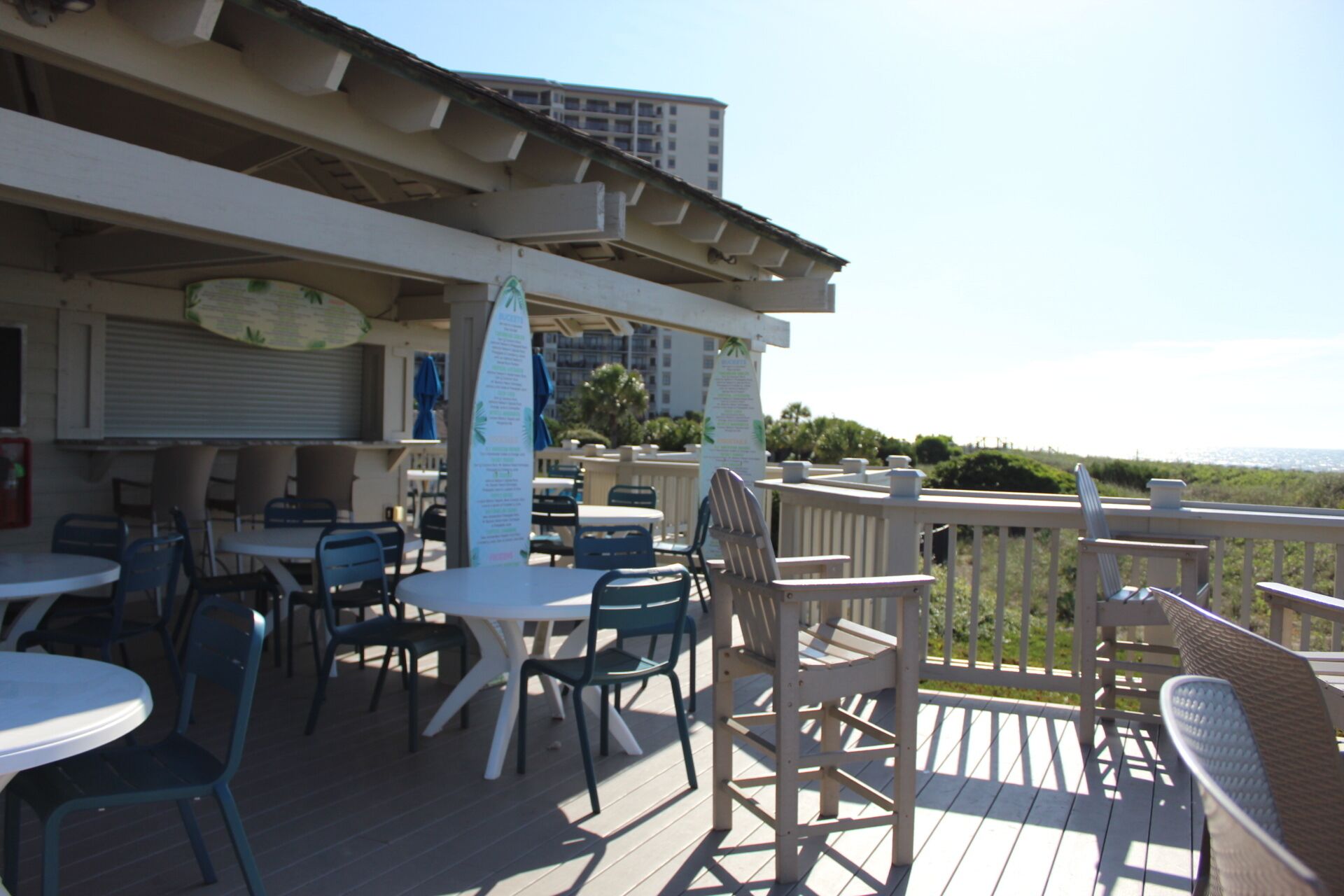 An outdoor patio with tables and chairs, a wooden deck, and a view of the ocean.