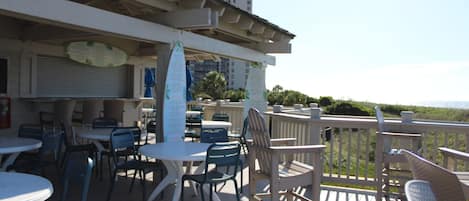 An outdoor patio with tables and chairs, a wooden deck, and a view of the ocean.