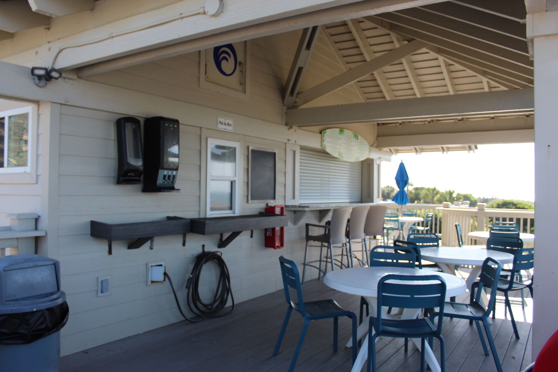 An outdoor patio area with a covered seating arrangement, including a table and chairs, and a trash bin.