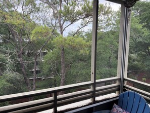 A room with a view of trees through a window, a wooden railing, and a blue chair. - One Bedroom Beach Oasis in Ocean Creek Resort (Myrtle Beach)