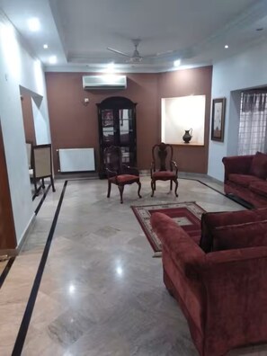 A spacious living room with a marble floor, two red sofas, a wooden cabinet, and a large window with curtains. - Cozy 2-bedroom ground portion-house in Islamabad, very central location (Islamabad)