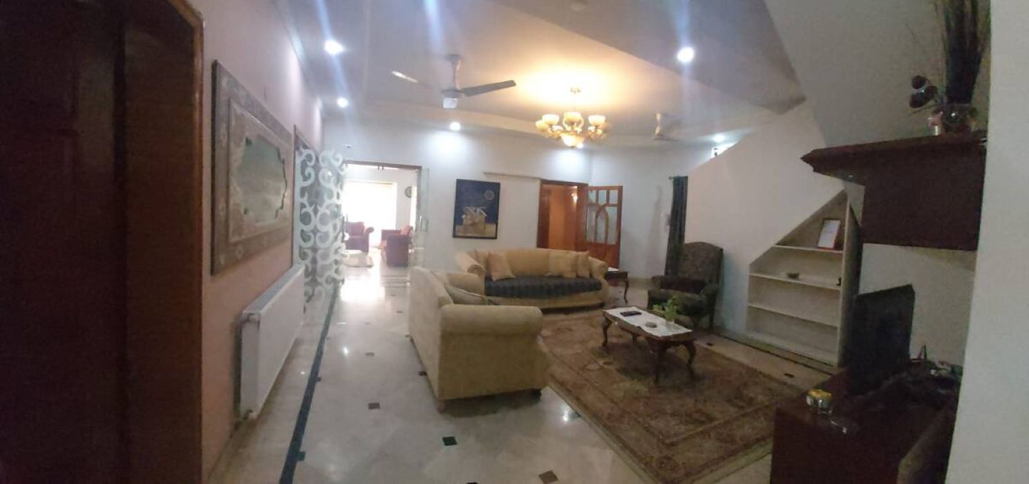 A spacious living room with a sofa, armchairs, and a coffee table. There is a chandelier and a ceiling fan.
