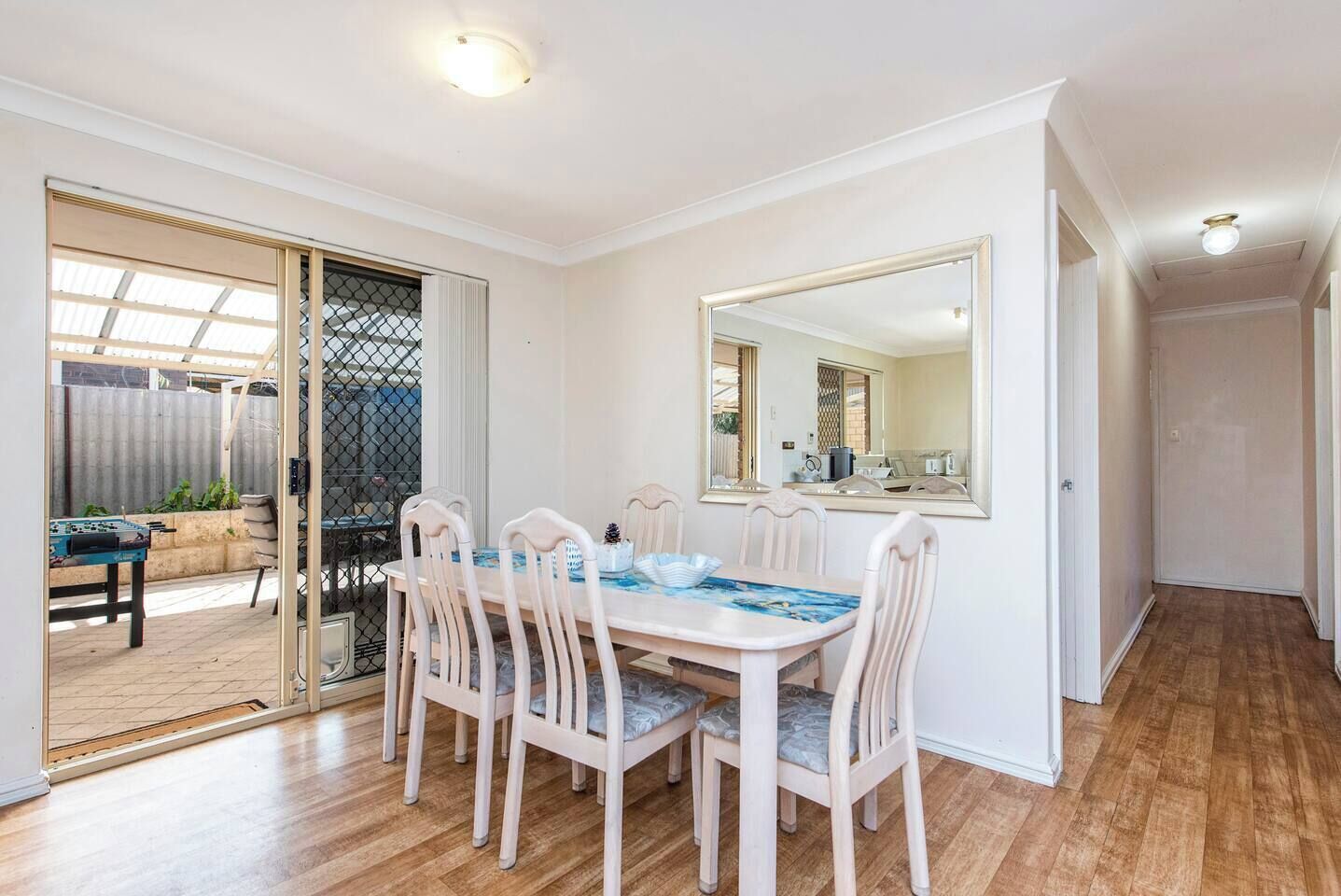 A dining area with a table and chairs, a large mirror, and a sliding glass door leading to an outdoor space with a foosball table.