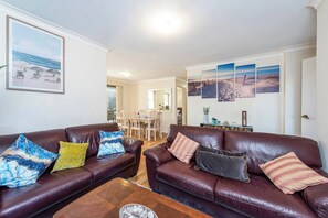 A living room with two leather sofas, a coffee table, and a dining area in the background. - Mandurah Coastal Getaway|Dolphins|Beaches|Sleeps 6 (Mandurah)