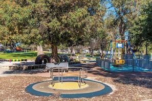 A park with a playground, a bench, and a tree. - Mandurah Coastal Getaway|Dolphins|Beaches|Sleeps 6 (Mandurah)
