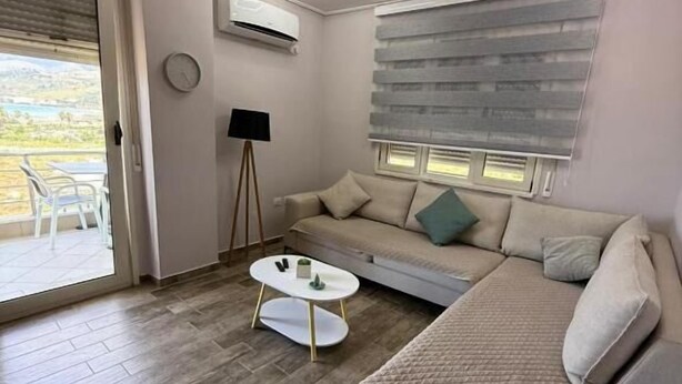 A modern living room with a sofa, a coffee table, and a window with blinds. - Coco Apartment (Radhimë)