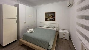 A bedroom with a bed, a wardrobe, a nightstand, and a painting on the wall. - Coco Apartment (Radhimë)