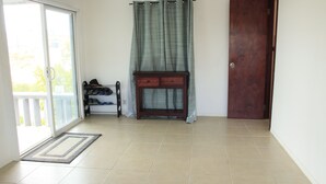A room with a sliding glass door leading to a balcony, a wooden console table with drawers, a dark wooden door, and a tiled floor.
