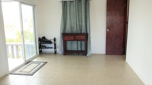 A room with a sliding glass door leading to a balcony, a wooden console table with drawers, a dark wooden door, and a tiled floor.
